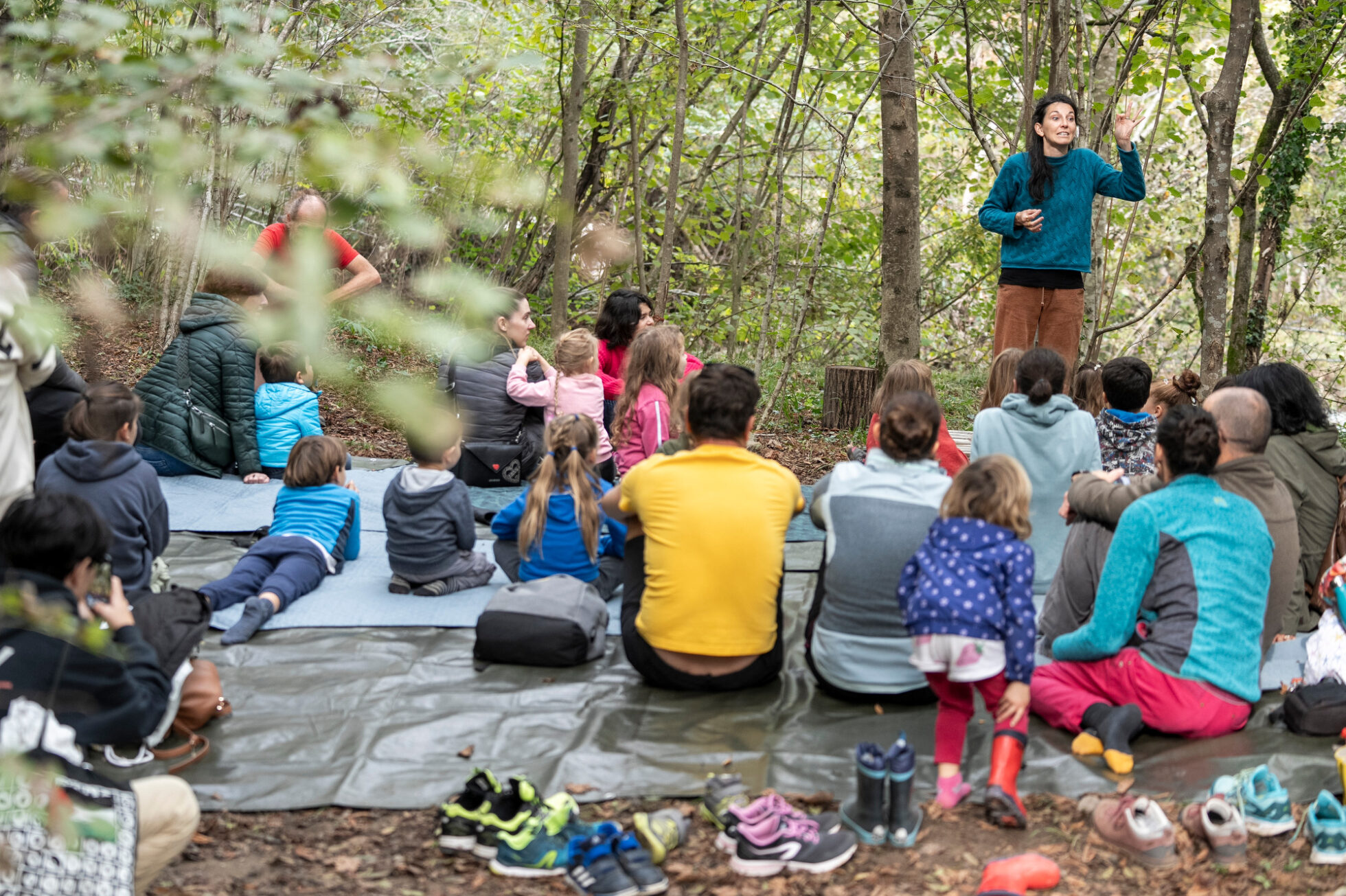 adulti e bambini seduti a terra partecipano ad uno spettacolo nel bosco